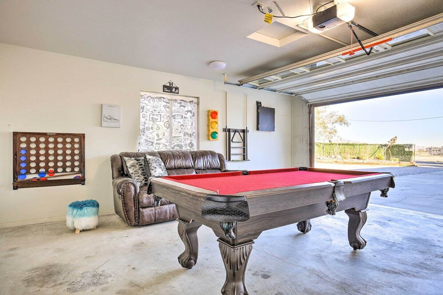 Une table de billard dans une pièce où se trouvent un canapé en cuir, une horloge murale et une porte donnant sur un garage.
