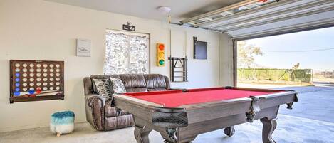 Une table de billard dans une piĂšce oĂč se trouvent un canapĂ© en cuir, une horloge murale et une porte donnant sur un garage.