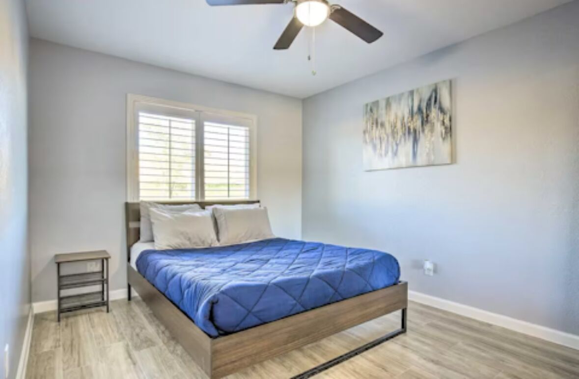 A bedroom with a bed, a ceiling fan, a window with blinds, and a painting on the wall.