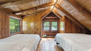 A cabin with two beds, wooden walls, and a sloped ceiling.