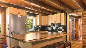 A modern kitchen with a central island, wooden cabinets, stainless steel appliances, and a seating area with leather stools.