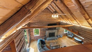 A log cabin interior with a fireplace, a sofa, a dining table, and a ceiling fan.