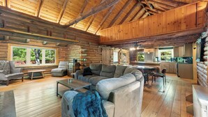 A log cabin interior with a living room, sofa, coffee table, and kitchen area.