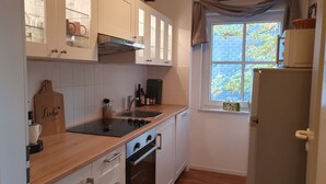 A compact kitchen with white cabinets, a black countertop, a built-in oven, a sink, and a window with a view of trees. - Harzblick apartment - your retreat in the middle of nature (Braunlage)