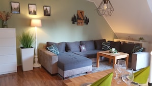 A cozy living room with a sectional sofa, a wooden coffee table, and a lamp. - Harzblick apartment - your retreat in the middle of nature (Braunlage)