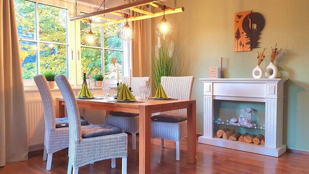 A dining area with a wooden table, wicker chairs, and a fireplace. - Harzblick apartment - your retreat in the middle of nature (Braunlage)