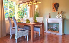 Un comedor con una mesa de madera, sillas de mimbre y una chimenea.