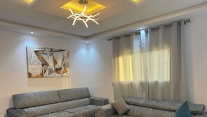 A modern living room with a sectional sofa, a glass coffee table, a contemporary light fixture, and a geometric abstract painting on the wall.