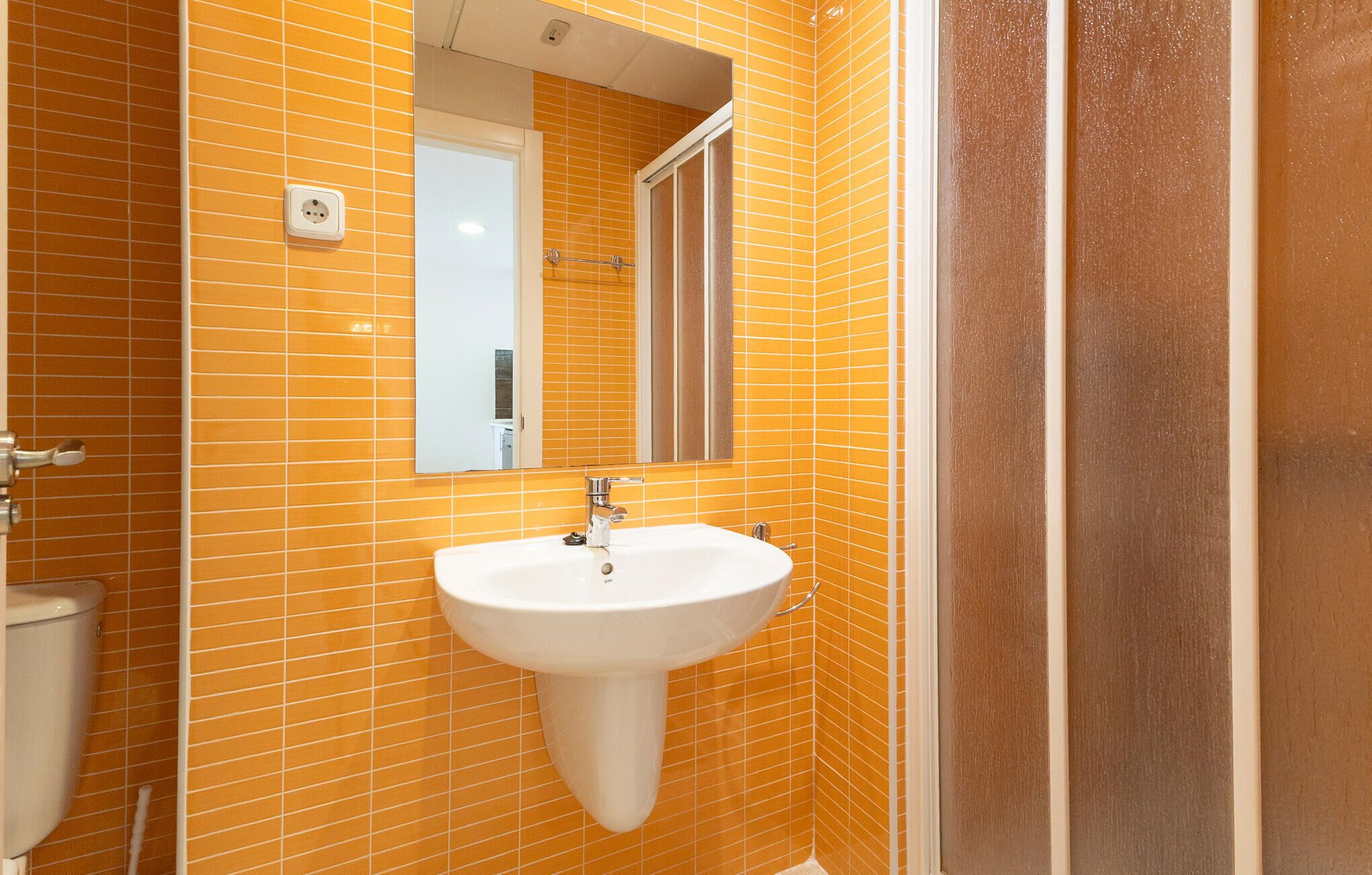 A bathroom with orange tiled walls, a white sink, and a mirror.
