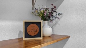Et indrammet motiverende citat på en træhylde, en hvid vase med blomster og en væg med struktur.