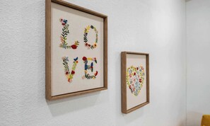 Two framed artworks on a wall, one spelling 'LOVE' with floral designs and the other a heart shape with flowers.