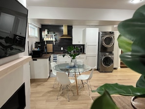 A modern kitchen with white cabinets, a glass dining table, and a built-in washer and dryer.