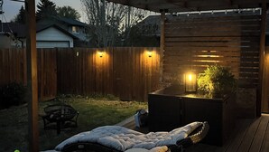 A covered outdoor patio with a pergola, two cushioned seating areas, a fire pit, and a small table. - Beautiful legal suite | Private sauna (Calgary)
