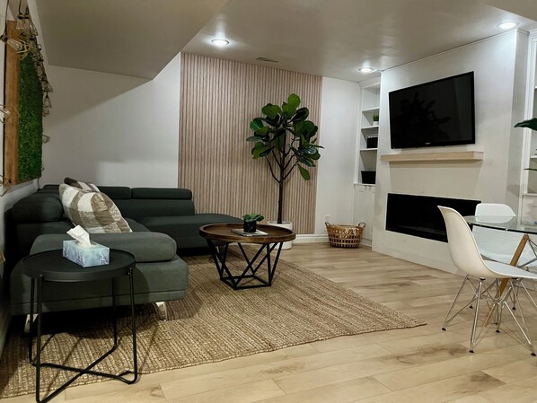 A modern living room with a sofa, a coffee table, a TV, and a dining area with a chair.
