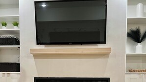 A modern living room with a flat-screen TV mounted above a fireplace. - Beautiful legal suite | Private sauna (Calgary)