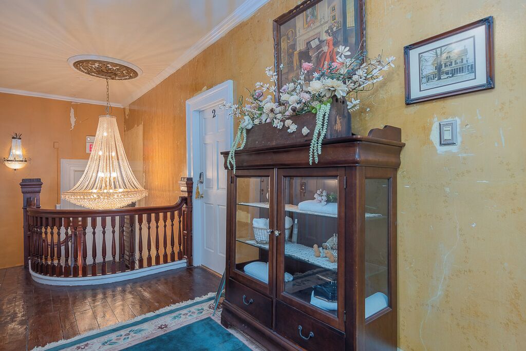 A grand foyer with a wooden staircase, a chandelier, a glass-fronted cabinet with decorative items, and a framed picture on the wall.