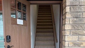 Una puerta de madera con un cartel, un muro de piedra y una escalera con alfombra que lleva al interior.