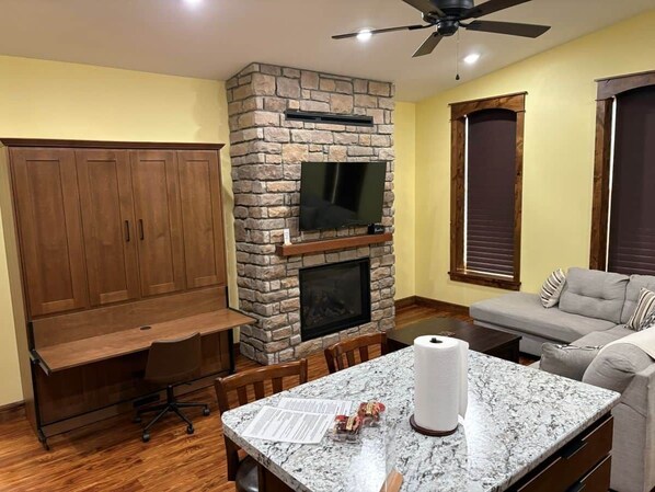 A living room with a stone fireplace, a flat-screen TV, a sofa, and a dining area with a table and chairs.
