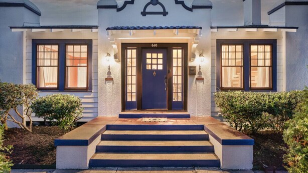 Una casa de dos pisos con una puerta azul, número 610, y un pequeño porche con escalones que llevan a la entrada.