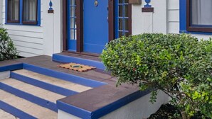 Un edificio blanco con puerta y ventanas azules, un pequeño porche, y el número "610" sobre la puerta.