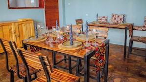 A dining area with wooden tables and chairs, set with plates, glasses, and cutlery. - Akagera Park Inn (Rwinkwavu)