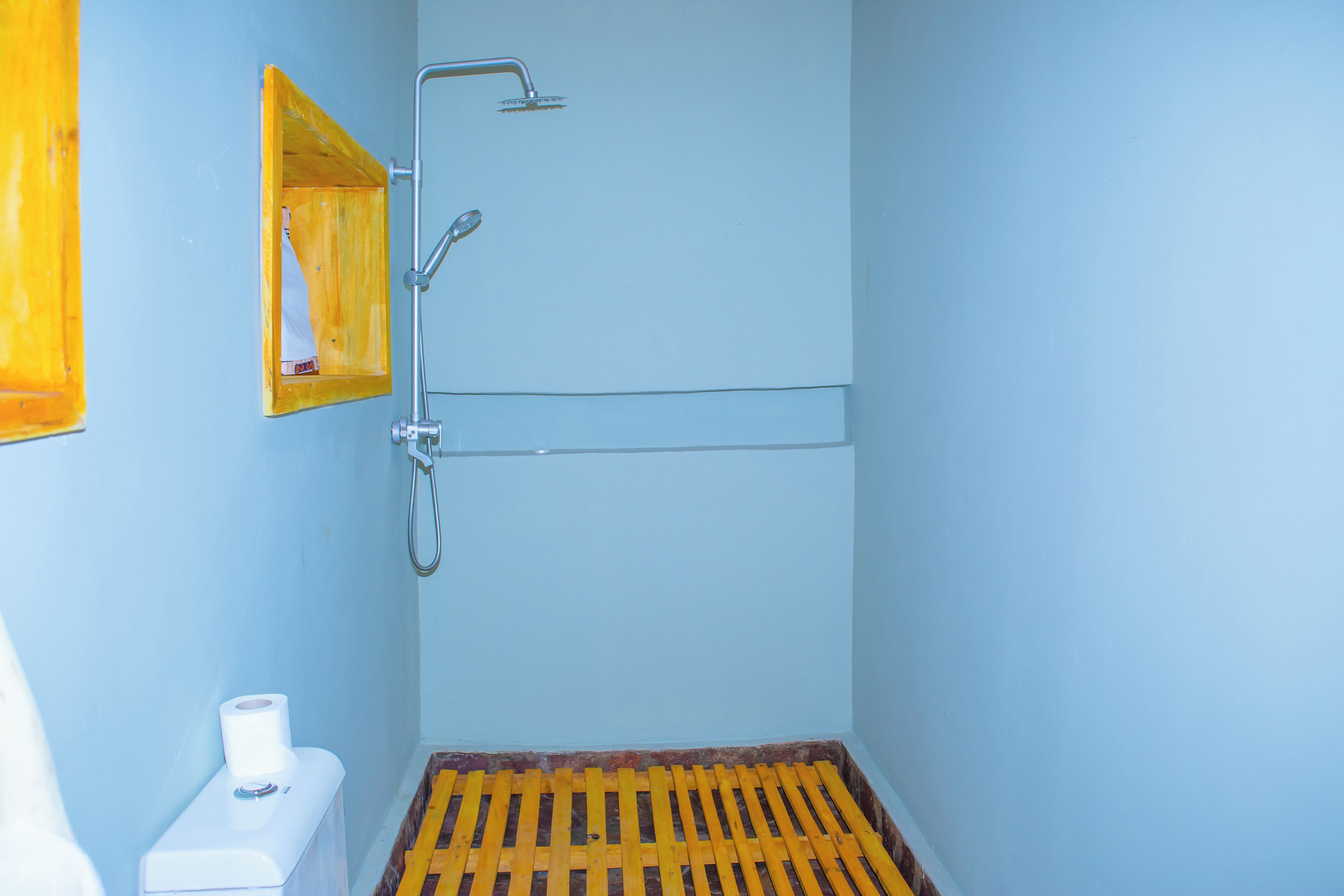 Un baño con ducha, inodoro y un estante de madera.