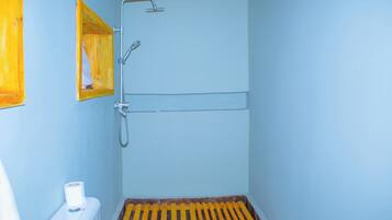 Un baño con ducha, inodoro y un estante de madera.