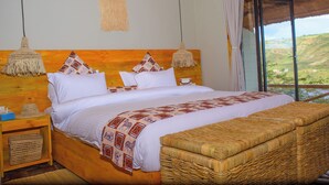 A bed with a patterned blanket, a wooden headboard, and a view of the outdoors through a large window. - Akagera Park Inn (Rwinkwavu)