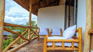 A wooden chair with white cushions in a covered outdoor area with stone flooring. - Akagera Park Inn (Rwinkwavu)
