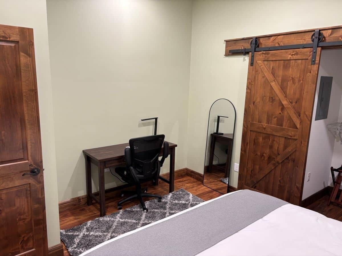 A bedroom with a bed, a desk, a chair, a mirror, and a sliding barn-style door.