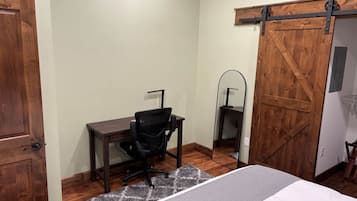 A bedroom with a bed, a desk, a chair, a mirror, and a sliding barn-style door.