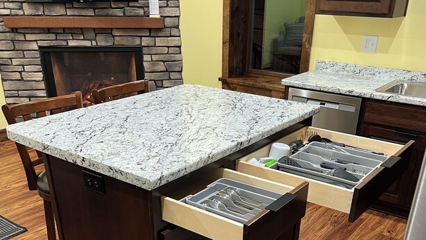 Une cuisine dotée d’un plan de travail en granit, de meubles en bois, d’une cuisinière encastrée et d’un lave-vaisselle.