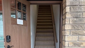 Une porte en bois avec une pancarte, un mur de pierre et un escalier recouvert de moquette menant à l’intérieur.