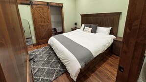 Une chambre à coucher comprenant un lit, une table de chevet, une tête de lit en bois, un placard avec une porte coulissante de style grange, et un ventilateur de plafond.