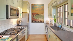 A compact kitchen with a gas stove, microwave, and a large poster of 'LA JOLLA'. - Ocean-View Retreat • Walk to La Jolla Cove & Village • Full Kitchen • Modern 1BR (La Jolla)