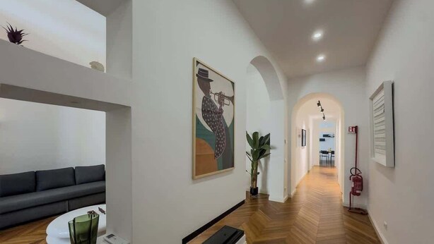 Ein moderner Flur mit Holzboden, einem schwarzen Sofa, einem weißen Couchtisch und einem Gemälde einer Person, die Trompete spielt.