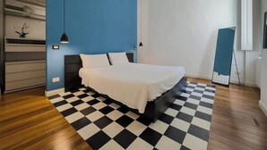 Ein Schlafzimmer mit einem Bett, einem Schachbrettmuster-Boden, einer blauen Akzentwand und einem Fenster mit Klimaanlage.