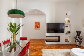 A modern living room with a glass dining table, red chairs, a large flat-screen TV, a green pendant light, and a white rug. - Casa Alessandria (Rome)