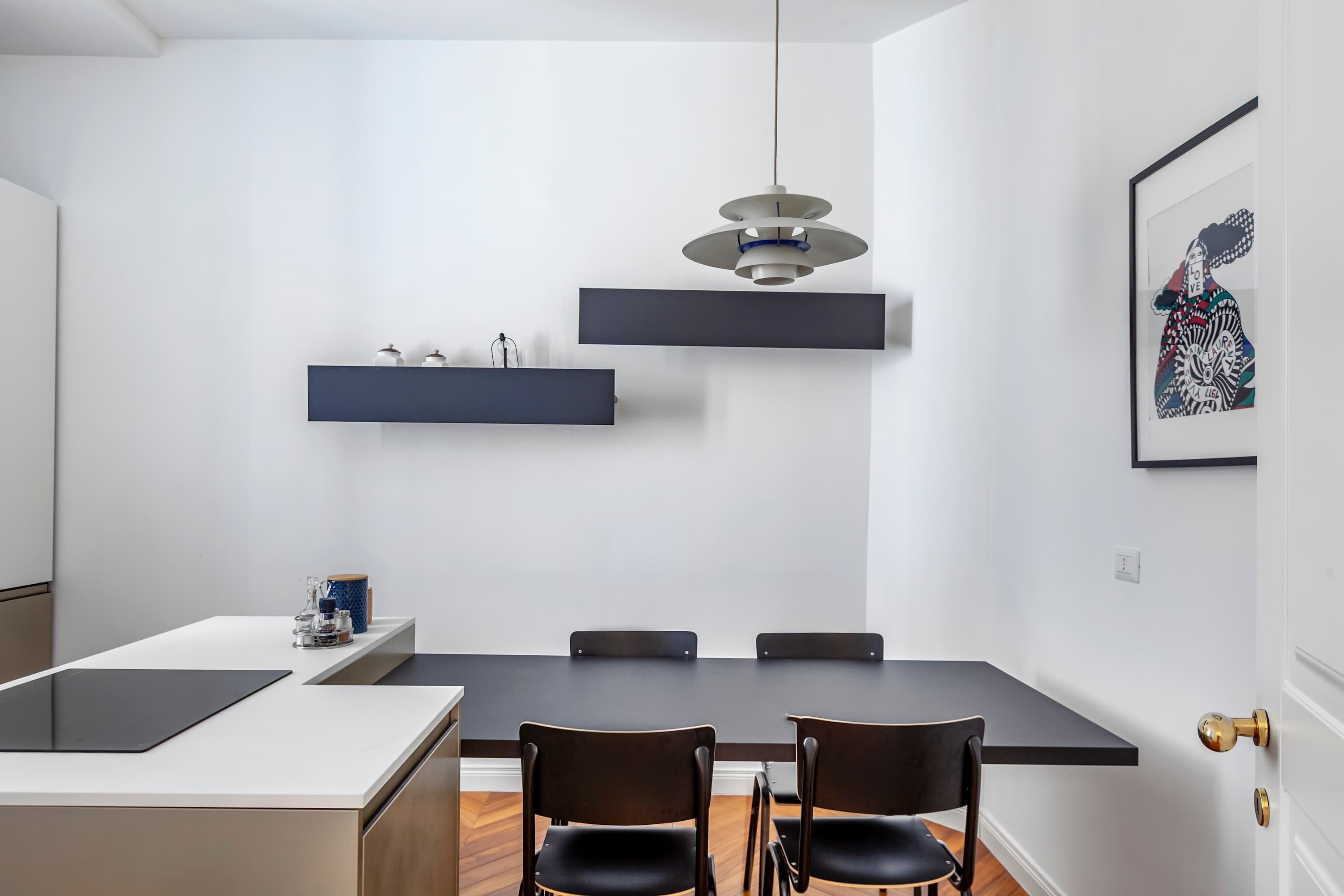 A modern dining area with a rectangular table, four chairs, a pendant light, and a wall-mounted shelf with jars.
