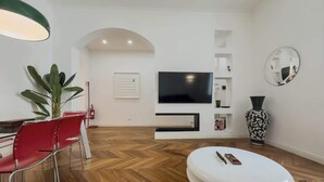 Ein modernes Wohnzimmer mit einem großen Flachbildfernseher, einem weißen Hocker, roten Sesseln, einer Topfpflanze und einer dekorativen Vase.