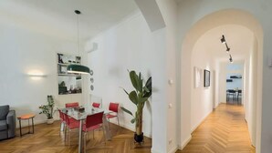 Ein geräumiger Wohnbereich mit Fischgrätparkett, einem Esstisch mit roten Stühlen, einem grauen Sofa und einer Topfpflanze.