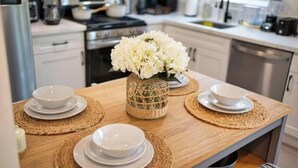 Una cocina con armarios blancos, una mesa de madera y un jarrón con flores blancas.