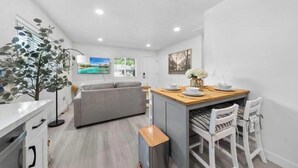Una cocina moderna con un sofá gris, mesa de comedor de madera y sillas blancas.