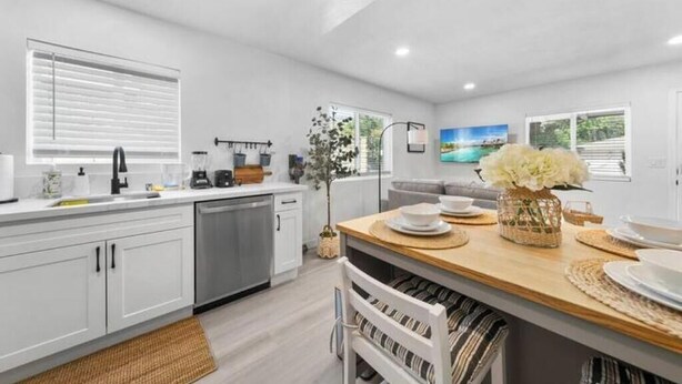 Una cocina moderna con armarios blancos, encimera de madera y un comedor con mesa lista para cuatro comensales.