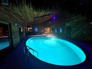 Ein großes Hallenbad mit Holzboden und -wänden, umgeben von Sitzbereichen und einer kleinen Poolbar.