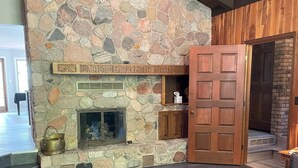 Una chimenea de piedra con repisa de madera, sofás de cuero y una puerta de madera.
