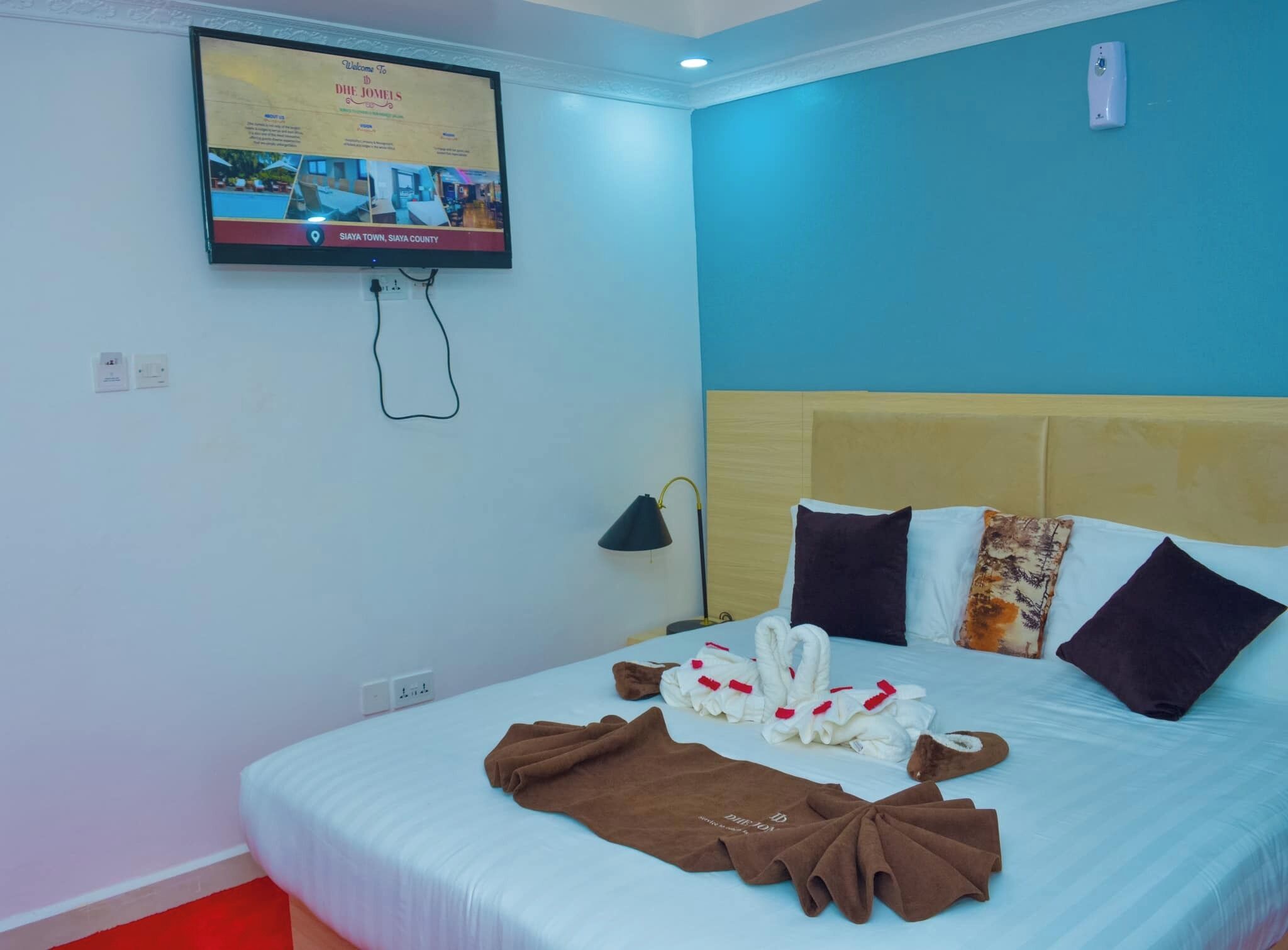 A hotel room with a bed, a TV mounted on the wall, and a nightstand with a lamp.