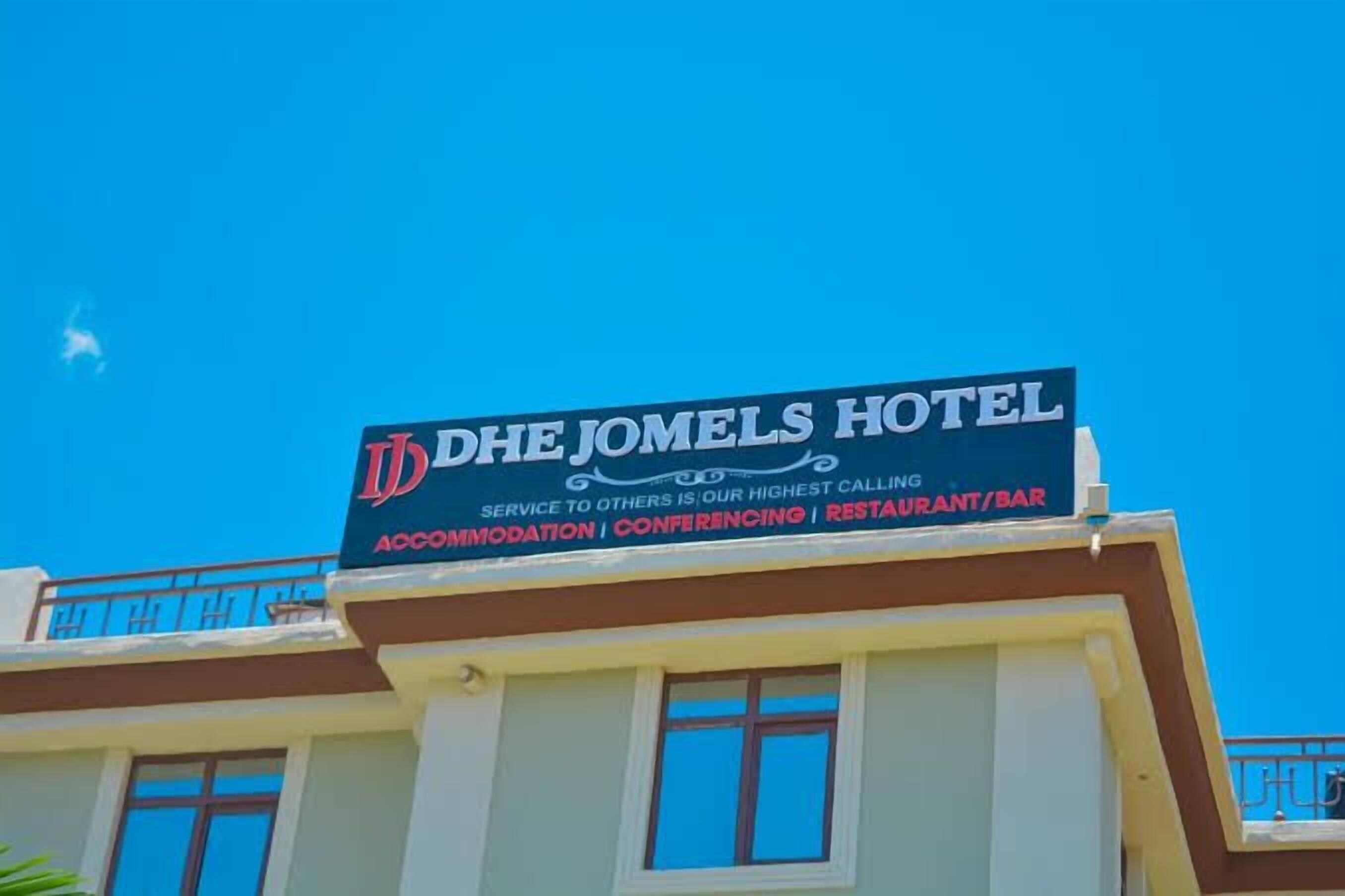 A hotel sign with the name "DHE JOMELS HOTEL" and mentions services like accommodation, conferencing, and a restaurant/bar.