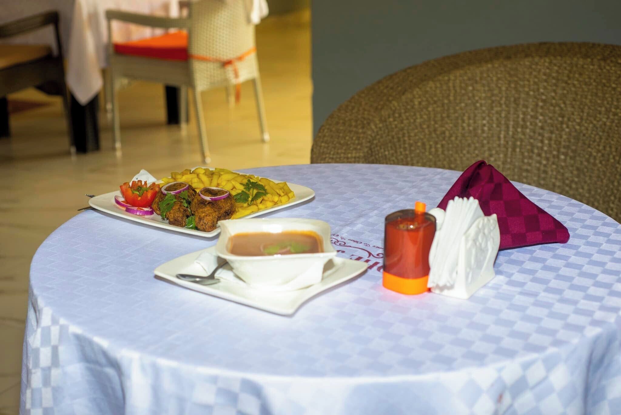 A round dining table with a checkered tablecloth, a plate of food, a bowl of soup, a glass of juice, and a napkin.