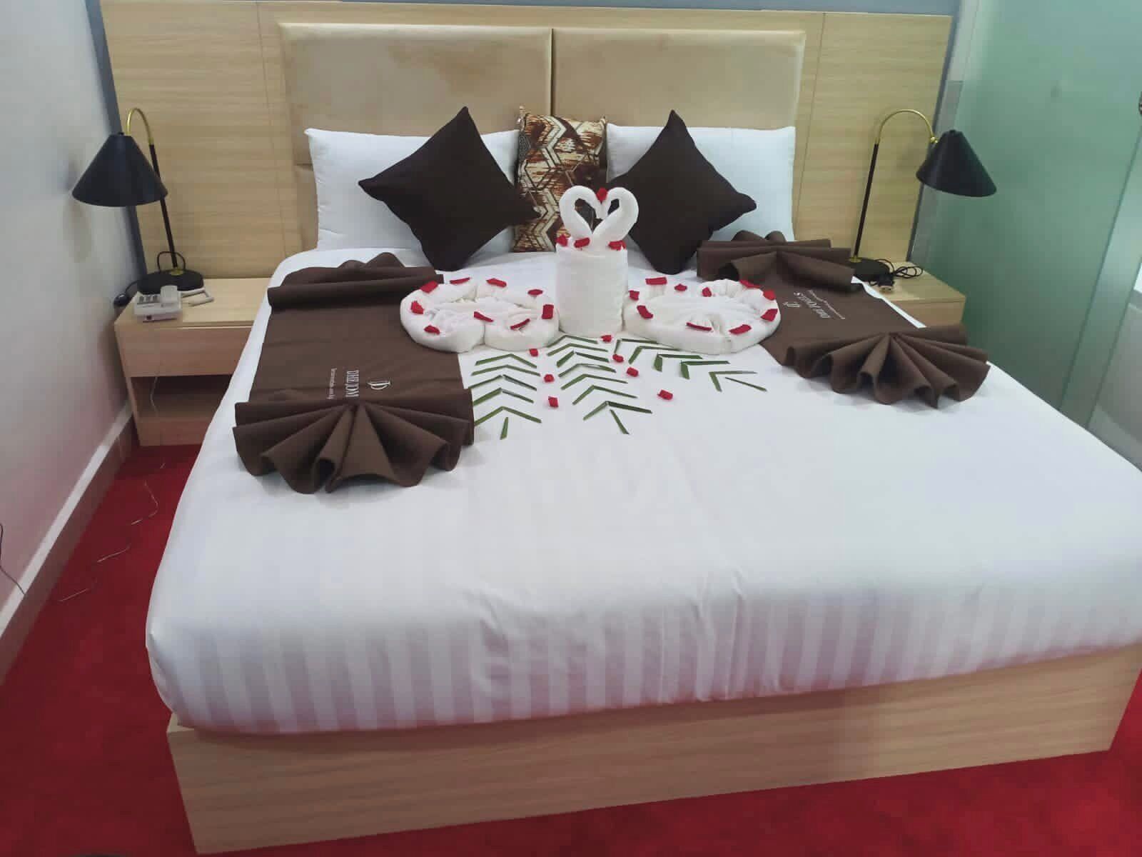 Una cama bien hecha con sábanas blancas, almohadas decorativas marrones y un centro de mesa con forma de cisne.